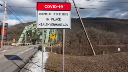 An image of a bridge in Vermont with a sign in front of it announcing a COVID-19 quarantine order.