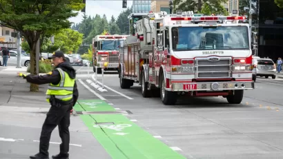 A police officer directs traffic as fire trucks arrive on scene along a street with green painted bike lanes.