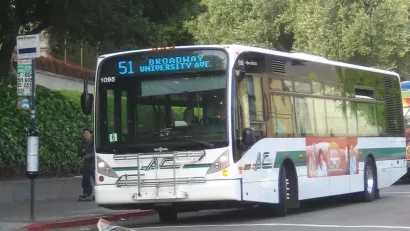White bus pulling up to sidewalk bus station in Berkeley, California.