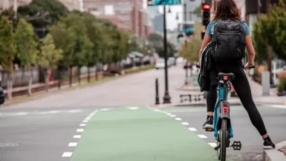 A person on a bike waits at an intersection by leaning against the curb.