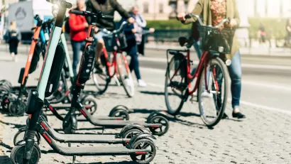 Parked electric scooters on a sidewalk with person walking bike in the background