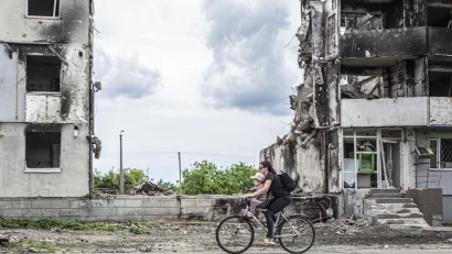 Woman and child ride bike past war-destroyed buildings in Borodyanka, Ukraine.