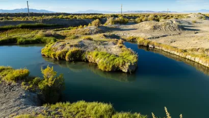 A hot springs in a low-lying desert area, with mountains in the distant background.
