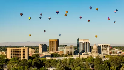Hot air balloons rise over Downtown Boise with the State Capitol building visible amidst the high rises.