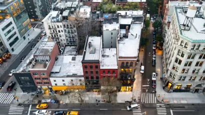 A block of the Bowery in New York City seen from high above, with taxis and other cars passing on the street in front of the buildings.