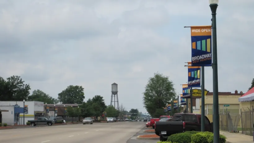 Wide, empty street with decorative town banners on light posts and water tower in background in West Memphis, Arkansas.