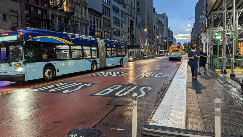 Blue and turquoise New York City bus at night on a red painted bus lane.