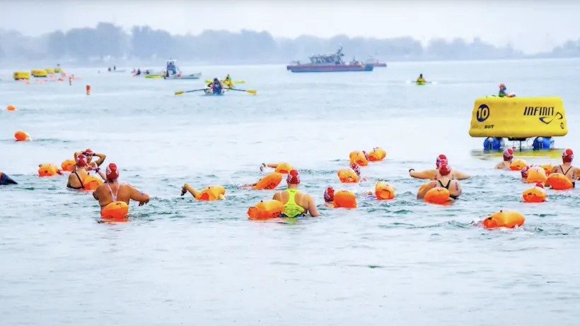 People in swim caps swimming in Chicago River wearing bright orange buoys.