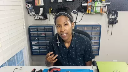 A Black woman works in a shop to prepare electronics for recycling..