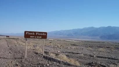 Brown and white "flash floods: next 55 miles" road sign in Death Valley, California