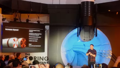 Elon Musk appears on stage in front of a backdrop of information about the Boring Company.