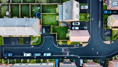 A suburban street in England, shown directly from above, with lush, green yards and driveways with cars parked in front.