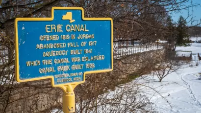 A commemorative plaque documents the history of the Erie Canal: Opened in 1819, abandoned fall of 1917, an extra aqueduct built in 1841 to expand the canal, and a canal park built in 1932.