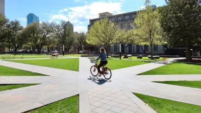 Woman rides bike on paved walkway through plaza in Fort Worth, Texas.