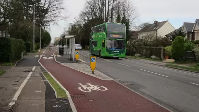 Red painted bike lane next to floating bus stop and green double-decker bus in the UK.