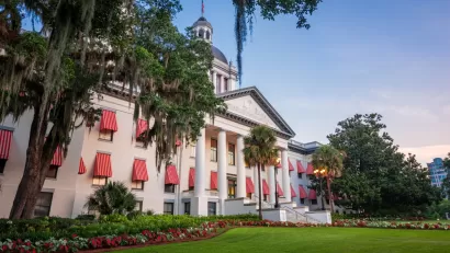 The buildings of the Florida State Capitol, old and new, are visible across a lawn in front of the old building.