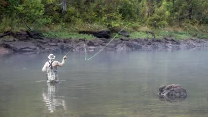 A fly fisher casts on a fog-covered river.