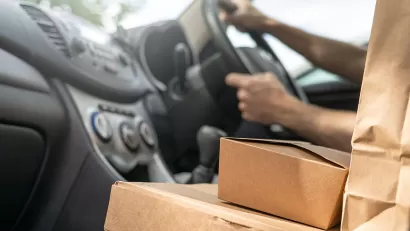 Close-up of cardboard food delivery boxes and bags on car seat next to driver.