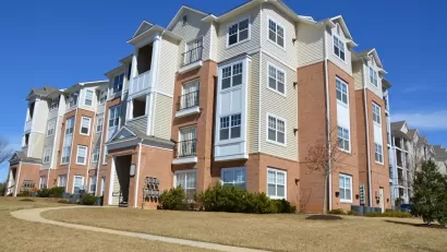 A large, four-story apartment building is surrounded by grass and concrete walkways.