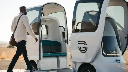 Man wearing sweater and messenger bag walking into white autonomous four-person Glydcar vehicle.