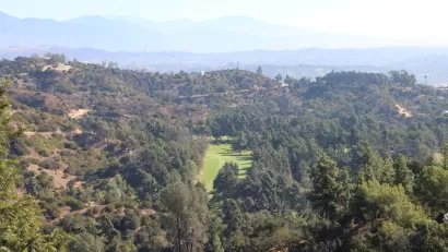 The fairway of a golf course is visible amidst the rolling hills of Griffith Park above Los Angeles.