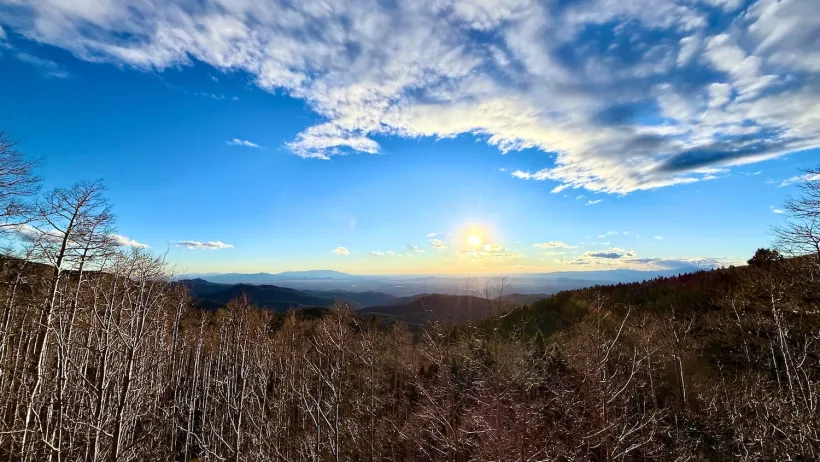 Sun rising over mountain forest with bright blue sky.