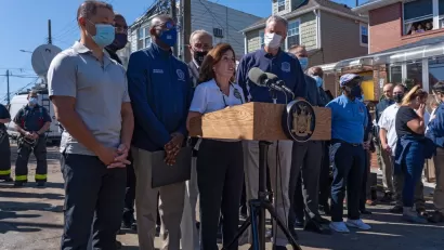 New York politicians, including Governor Kathy Hochul and Mayor Bill de Blasio, gather in front of microphones for a press conference.