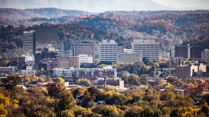 An aerial view of downtown Knoxville, Tennessee, with rolling hills and autumn foliage in the background.