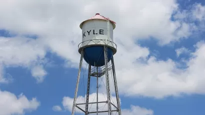 White water tower with KYLE text against blue sky with white clouds.
