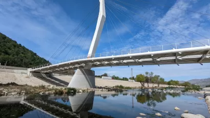A cable-stayed bridge designed spans the water of the Los Angeles River, which is placid and dotted with rocks.
