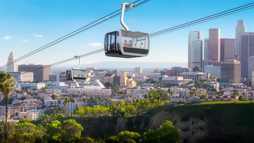 Rendering of aerial gondola in air above Los Angeles with City Hall building and downtown skyline visible in background.