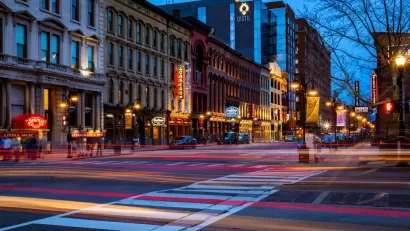 A Downtown Louisville street at night, with the lights of passing shown with a blurred effect.