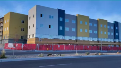 White, yellow, gray boxy apartment building with construction fence surrounding bottom floor in Albuquerque, New Mexico.