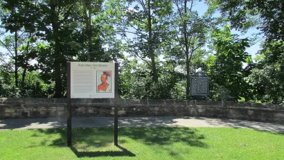 Informational plaque in front of paved walkway next to tall green trees in Black Hawk State Historic Site, Illinois.