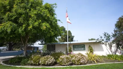 Small white one-story building with Maggie Hathaway Golf Course sign with American flag on flagpole and green lawn