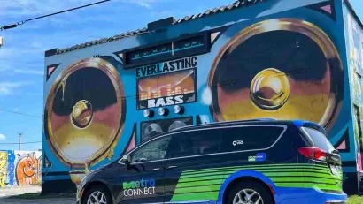 Black and green MetroConnect microtransit van in front of mural of boom box on Miami building.
