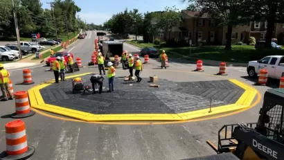 Workers in safety vests installing a black modular roundabout ringed with yellow.