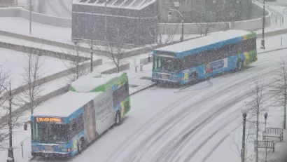 Two buses pull up to a station on a snowy day.