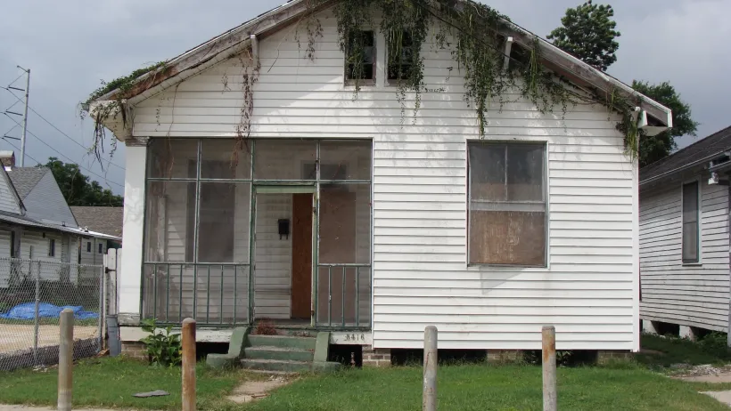 Small white wood house with boarded up windows in New Orleans, Louisiana with moss growing down from roof.