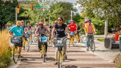 Group of people riding Pacers Bikeshare bikes on a tree-lined paved path.