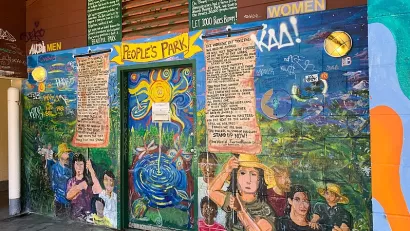 Colorful mural depicting people holding signs with proclamations on exterior wall of public restroom in People's Park, Berkeley