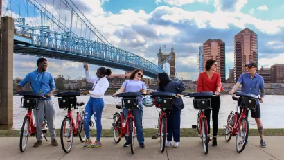 Six people posing with Red Bike bike share bikes with bridge and river in background.