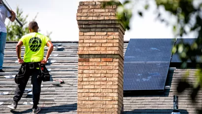 Roofers stand on top of a residential roof while installing solar panels.