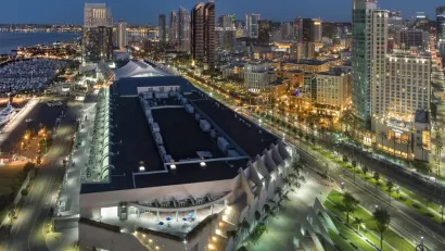The San Diego Convention Center is illuminated at night with the backdrop of public transit lines and high-rise buildings.