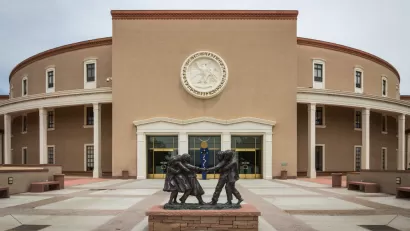 The New Mexico State Capitol building, with a statue of small children playing in the foreground.