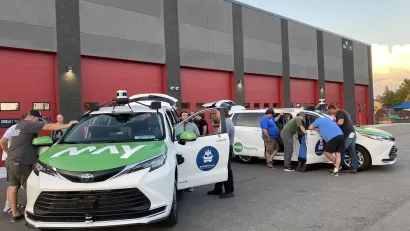 People examining parked goMARTI vans at launch event
