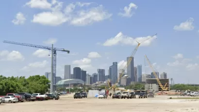 Dirt lot with construction cranes and parked cars with downtown Houston skyline in background