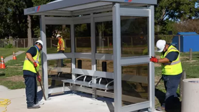 Workers in yellow safety vests installing a bus station shelter in Houston, Texas.