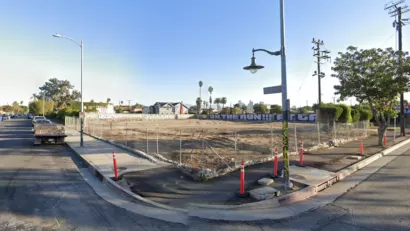 Google street view of vacant fenced-in dirt lot in South Los Angeles with graffiti on wall in background.