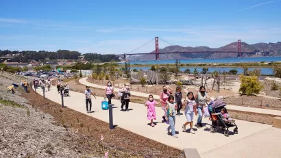 People walking on a concrete pathway at Presidio Tunnel Tops with the Golden Gate Bridge in the background